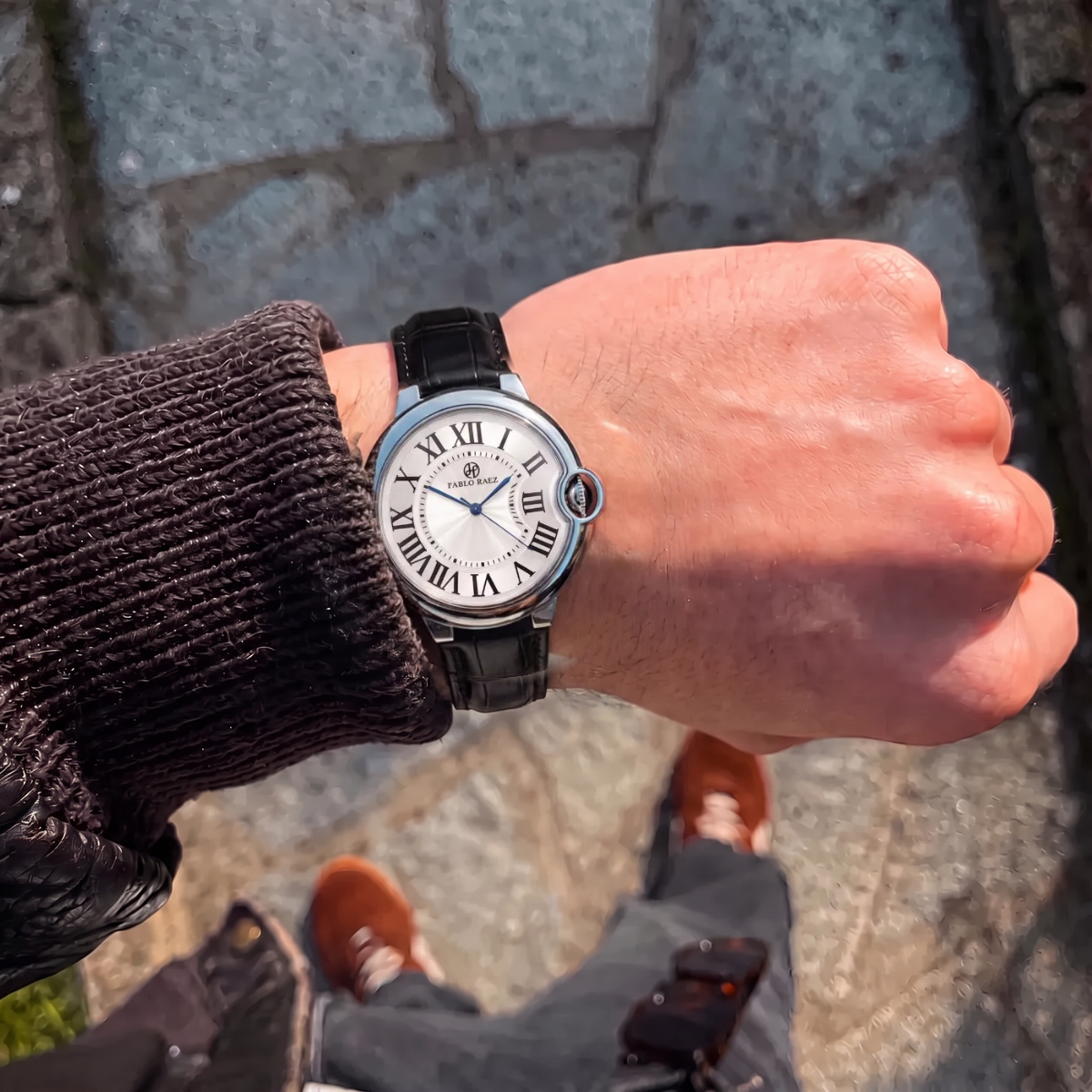 Murray 36mm watch with black leather strap on a man's wrist, seen from above on a cobblestone street #color_black
