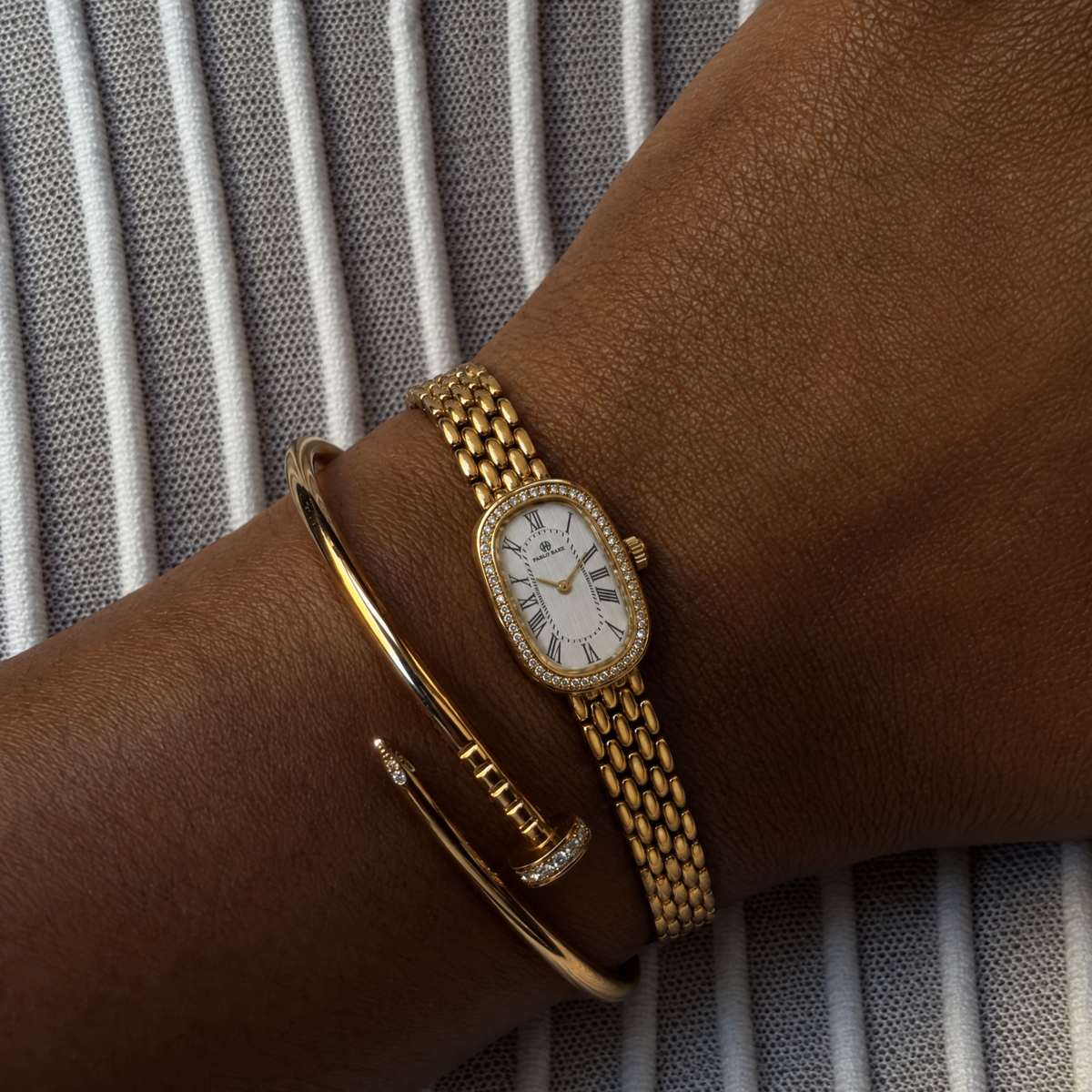 Belgrave 21mm gold women's watch worn on the wrist with slim gold bangles #color_gold