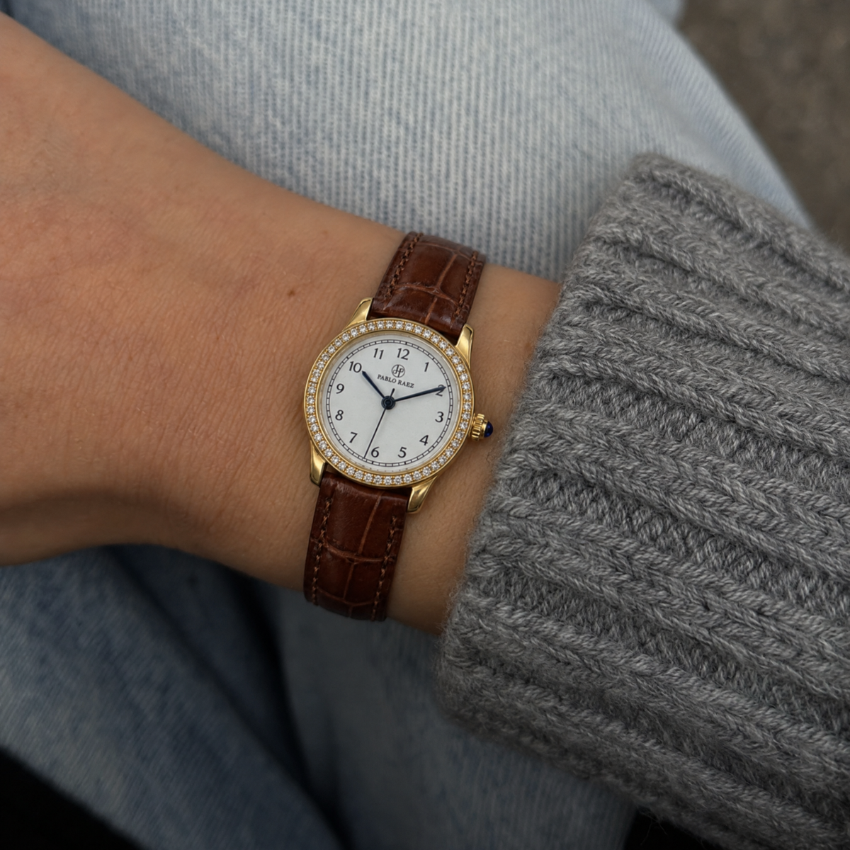 Mayfair 28mm gold women's watch with brown leather strap worn on the wrist with a grey knit sleeve #color_brown